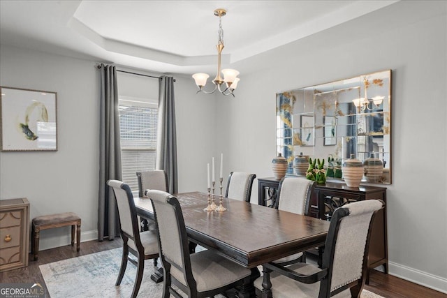 dining space featuring dark wood-type flooring, a notable chandelier, and a tray ceiling