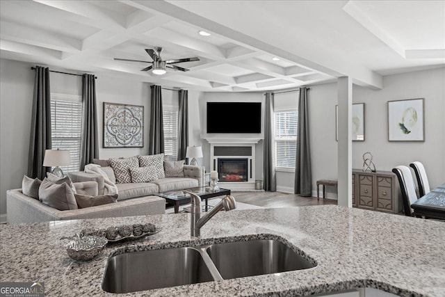 living room with coffered ceiling, sink, light wood-type flooring, ceiling fan, and beam ceiling