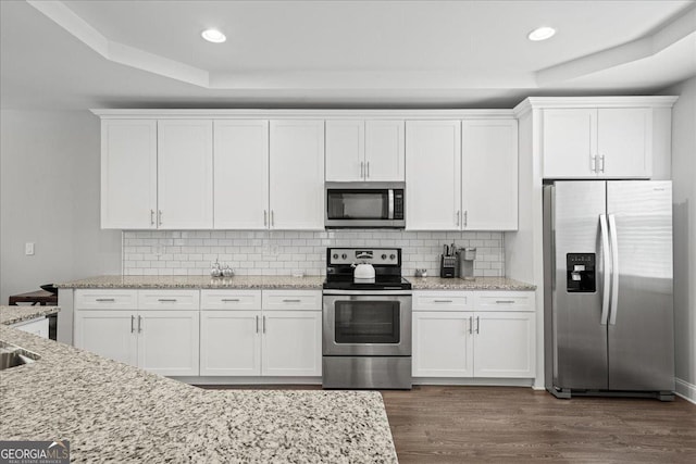 kitchen with stainless steel appliances, white cabinetry, and light stone countertops