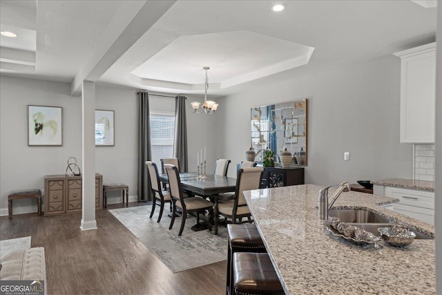 dining room with a raised ceiling, sink, dark wood-type flooring, and a chandelier