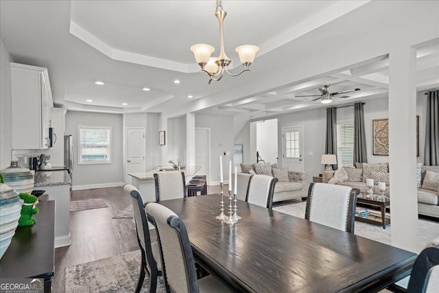 dining space with dark wood-type flooring, coffered ceiling, sink, beam ceiling, and ceiling fan with notable chandelier