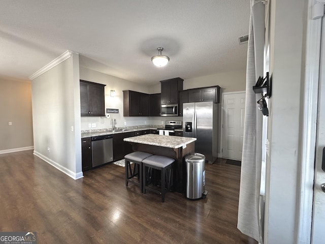 kitchen with sink, a breakfast bar area, appliances with stainless steel finishes, dark hardwood / wood-style floors, and a center island