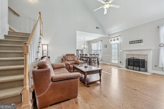 living room featuring ceiling fan with notable chandelier, a fireplace, high vaulted ceiling, and light wood-type flooring