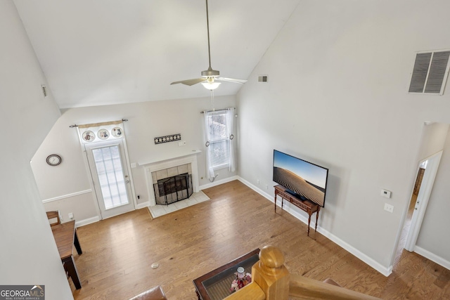 living room featuring hardwood / wood-style flooring, ceiling fan, high vaulted ceiling, and a tile fireplace