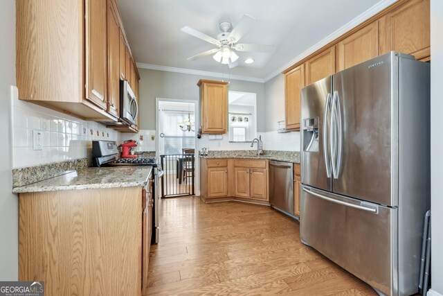 kitchen with sink, light stone counters, crown molding, light hardwood / wood-style flooring, and stainless steel appliances