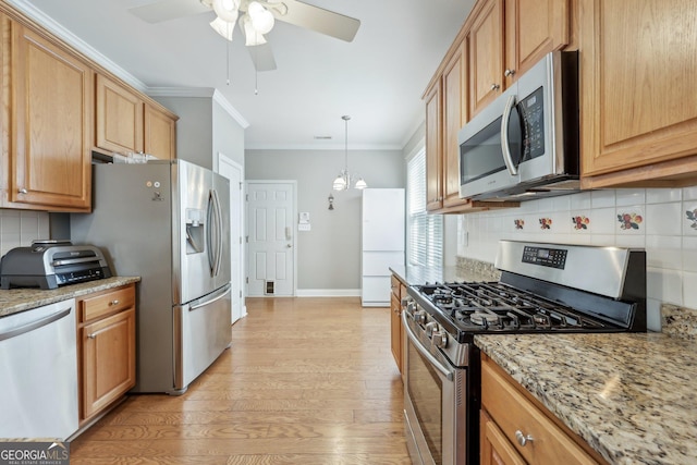 kitchen with pendant lighting, light stone counters, ornamental molding, and appliances with stainless steel finishes