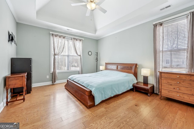 bedroom featuring crown molding, ceiling fan, a tray ceiling, and light wood-type flooring