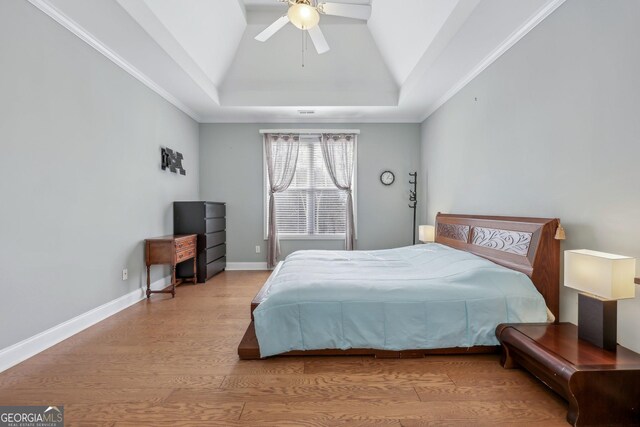 bedroom with crown molding, ceiling fan, a raised ceiling, and light hardwood / wood-style flooring