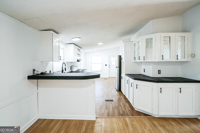 kitchen featuring stainless steel fridge, lofted ceiling, white cabinets, and kitchen peninsula