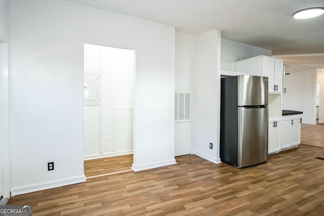 kitchen featuring white cabinetry, hardwood / wood-style floors, a textured ceiling, and stainless steel refrigerator