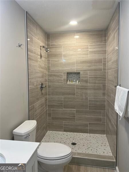 bathroom with tiled shower, vanity, and toilet