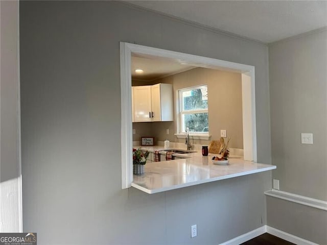 kitchen with white cabinetry, crown molding, kitchen peninsula, and sink