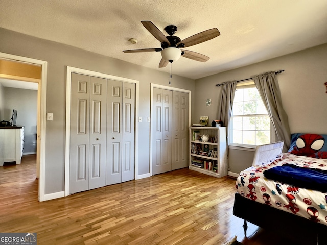 bedroom featuring ceiling fan, two closets, a textured ceiling, and light wood-type flooring