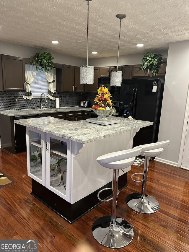 kitchen with pendant lighting, sink, dark hardwood / wood-style floors, light stone counters, and a kitchen island