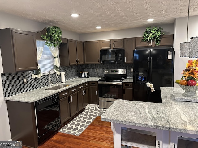 kitchen featuring wood finished floors, decorative backsplash, a sink, light stone countertops, and black appliances