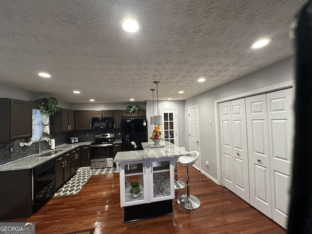 kitchen featuring a sink, a kitchen breakfast bar, backsplash, black appliances, and dark wood finished floors