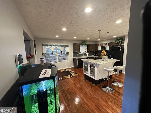 kitchen featuring a center island, dark wood finished floors, backsplash, freestanding refrigerator, and a kitchen bar