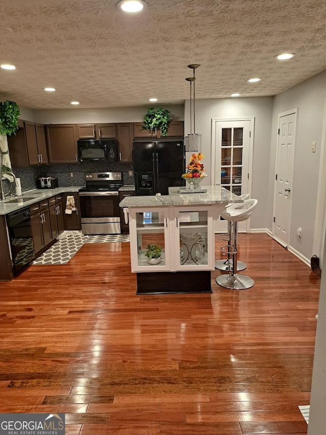 kitchen featuring hardwood / wood-style flooring, black appliances, tasteful backsplash, and a sink