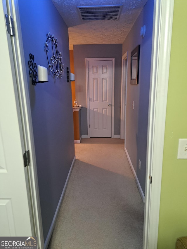 hallway featuring light carpet, a textured ceiling, visible vents, and baseboards