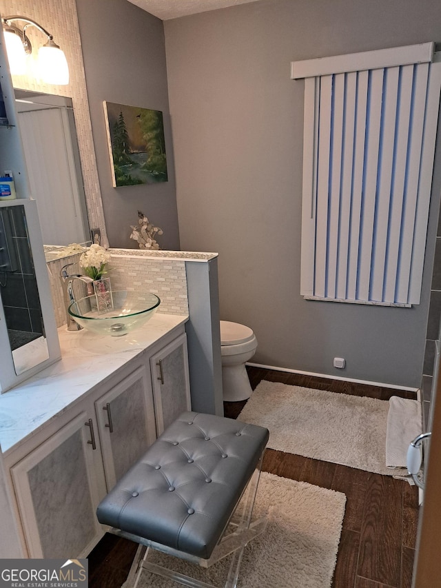 bathroom featuring toilet, wood finished floors, vanity, baseboards, and backsplash