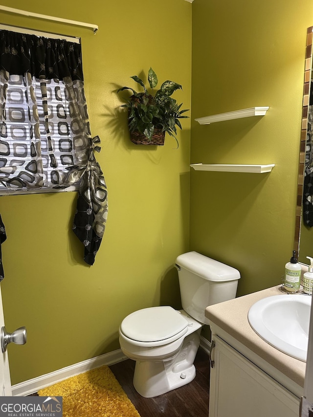 bathroom featuring toilet, baseboards, wood finished floors, and vanity