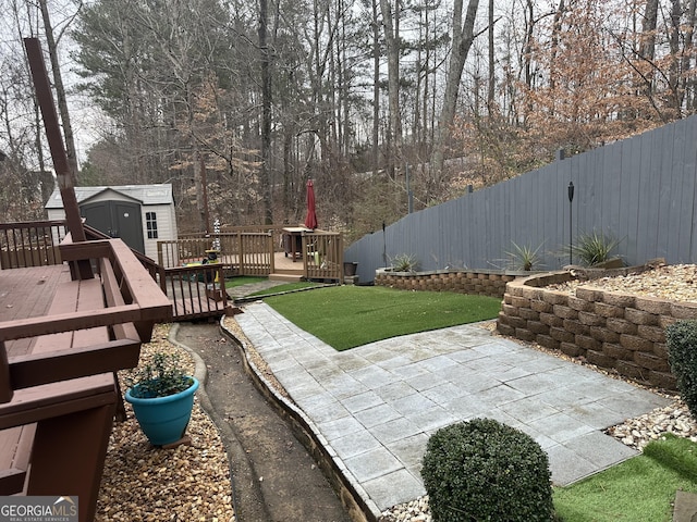 view of yard featuring an outbuilding, a deck, a fenced backyard, a storage unit, and a patio area