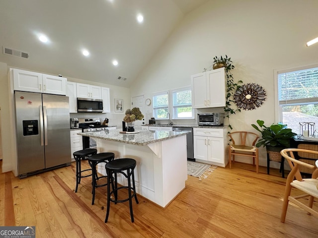 kitchen featuring appliances with stainless steel finishes, white cabinetry, light stone countertops, light hardwood / wood-style floors, and a kitchen island