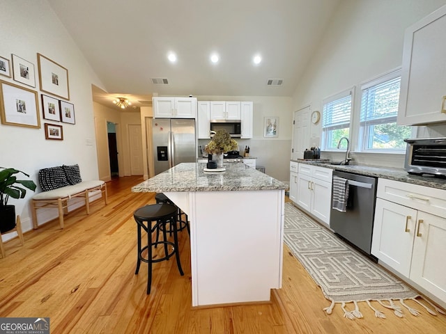 kitchen with sink, stainless steel appliances, light stone countertops, white cabinets, and a kitchen island