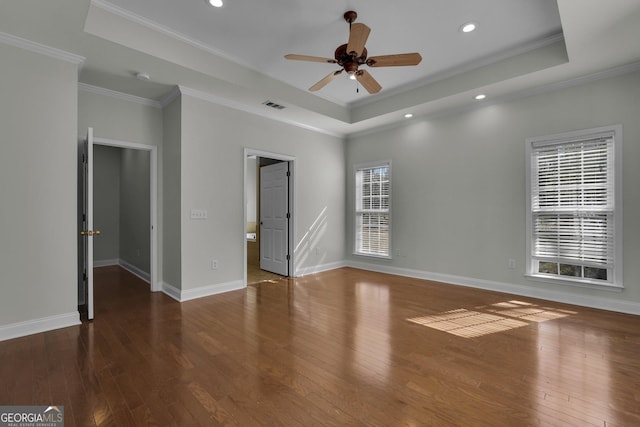 empty room with dark wood-type flooring, ceiling fan, ornamental molding, and a raised ceiling