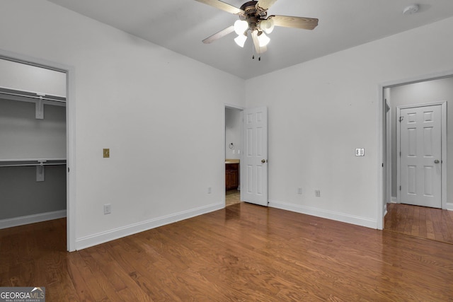 unfurnished bedroom featuring ensuite bathroom, wood-type flooring, a walk in closet, ceiling fan, and a closet