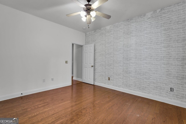 empty room with ceiling fan, wood-type flooring, and brick wall