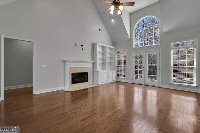 unfurnished living room with french doors, high vaulted ceiling, ceiling fan, a fireplace, and hardwood / wood-style floors