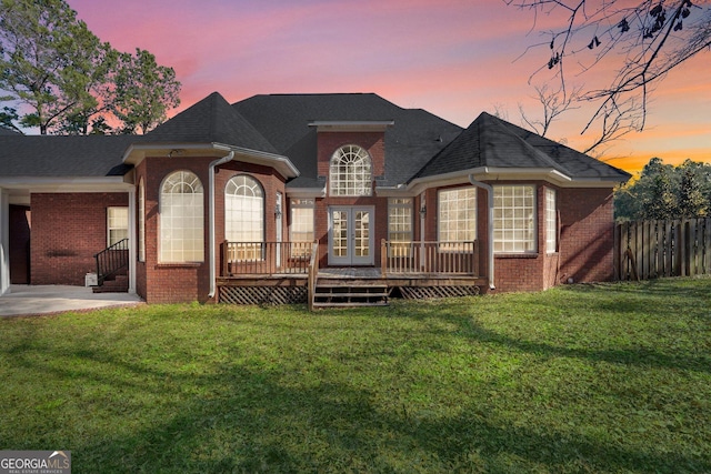 back house at dusk featuring a wooden deck, a lawn, and french doors