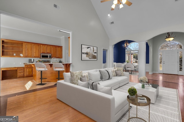 living room with high vaulted ceiling, decorative columns, sink, ceiling fan, and light hardwood / wood-style flooring