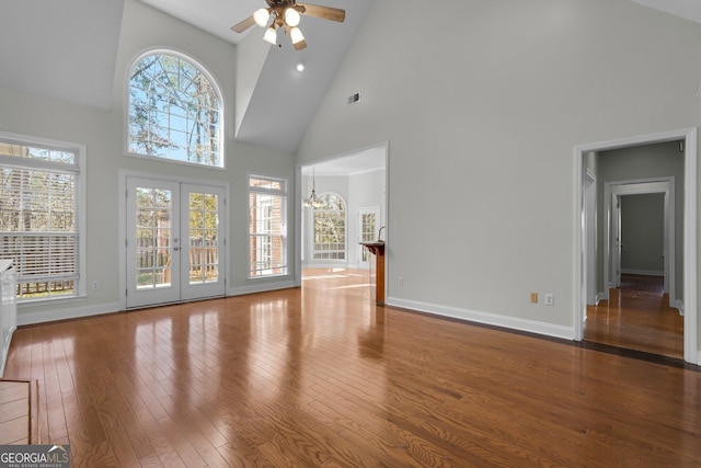 unfurnished living room featuring a wealth of natural light, ceiling fan with notable chandelier, hardwood / wood-style floors, and french doors