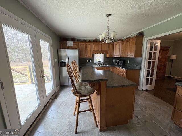 kitchen with a kitchen island, pendant lighting, stainless steel fridge, an inviting chandelier, and french doors