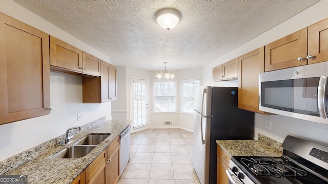 kitchen with sink, appliances with stainless steel finishes, hanging light fixtures, light stone counters, and a chandelier