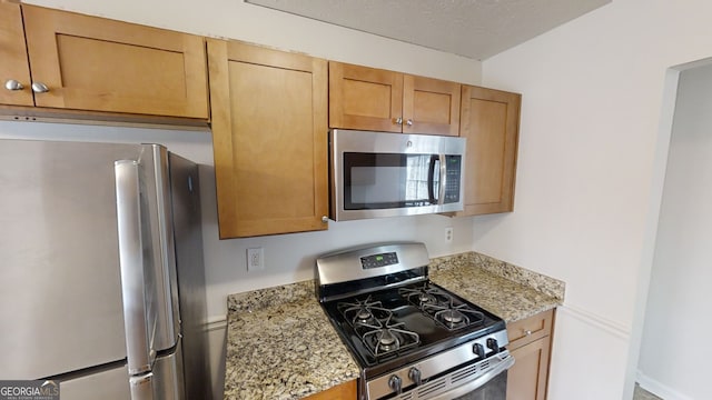 kitchen featuring stainless steel appliances, a textured ceiling, and light stone counters