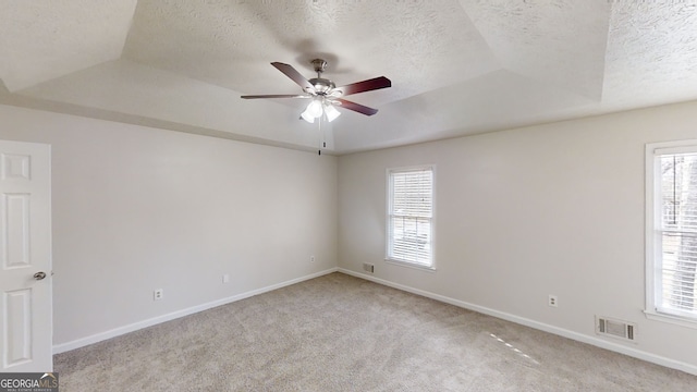 carpeted empty room with a raised ceiling, ceiling fan, a healthy amount of sunlight, and a textured ceiling