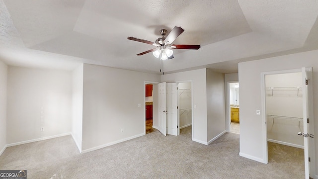 unfurnished bedroom featuring a raised ceiling, a spacious closet, and light colored carpet