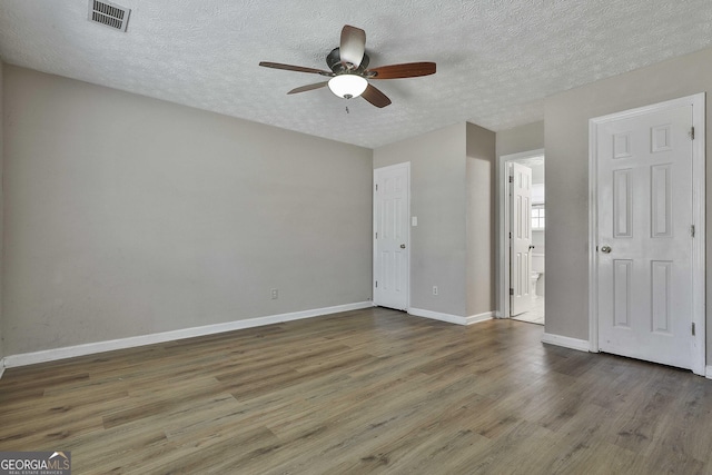 unfurnished bedroom with ceiling fan, dark hardwood / wood-style floors, connected bathroom, and a textured ceiling