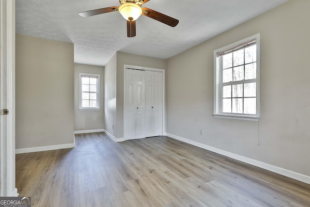 unfurnished bedroom featuring ceiling fan, a closet, light hardwood / wood-style flooring, and a textured ceiling