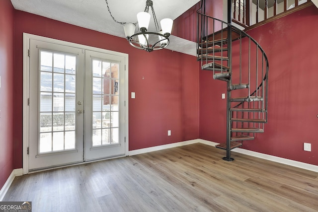 unfurnished dining area with a notable chandelier, hardwood / wood-style flooring, and french doors