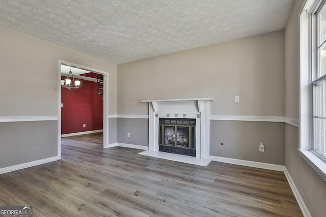 unfurnished living room with a tile fireplace, plenty of natural light, wood-type flooring, and a notable chandelier