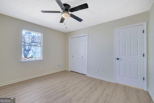 unfurnished bedroom with ceiling fan, a textured ceiling, light wood-type flooring, and a closet