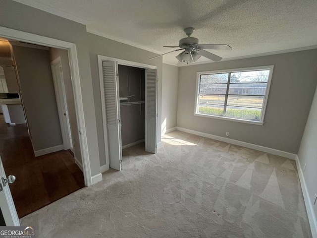 unfurnished bedroom with ornamental molding, light colored carpet, ceiling fan, a textured ceiling, and a closet