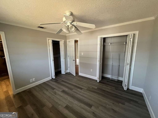 unfurnished bedroom featuring ornamental molding, dark hardwood / wood-style floors, and two closets