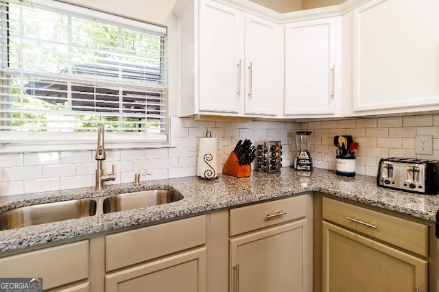 kitchen featuring tasteful backsplash, sink, light stone counters, and white cabinets