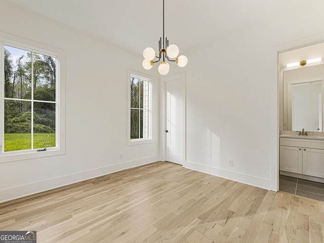 unfurnished room with light hardwood / wood-style flooring, sink, a notable chandelier, and plenty of natural light