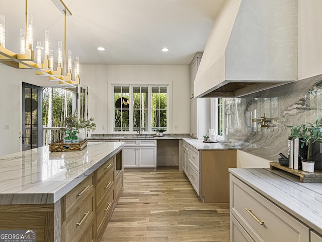 kitchen with sink, hanging light fixtures, light stone countertops, light hardwood / wood-style floors, and custom exhaust hood